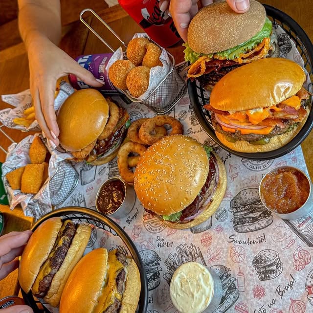 Mesa com hambúrgueres, porções e molhos Óia Burguer